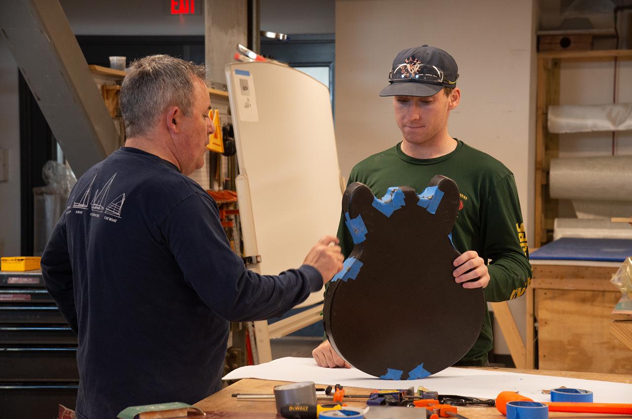 Instructor and student discussing a carbon fiber component in a workshop.