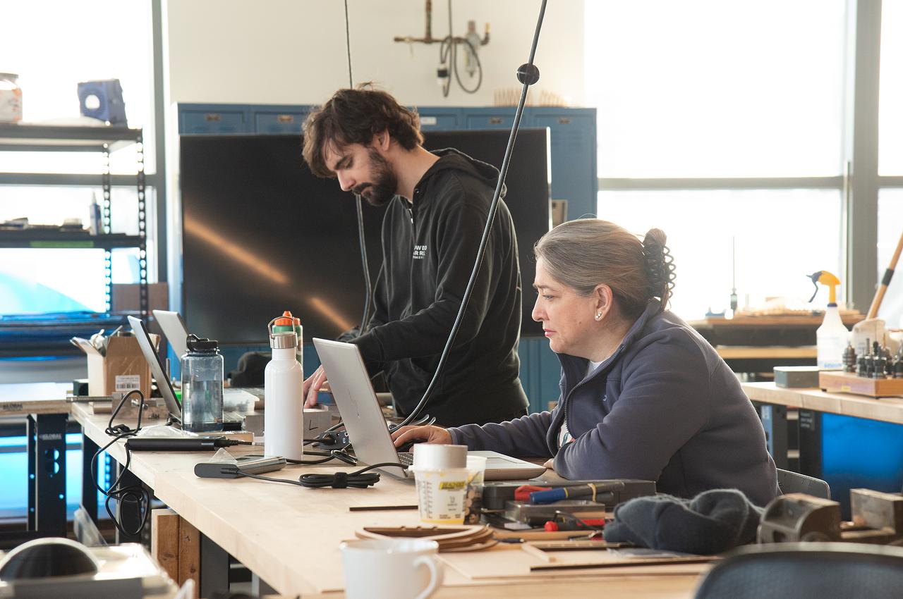 Two people collaborating on a design project using laptops in a workshop.