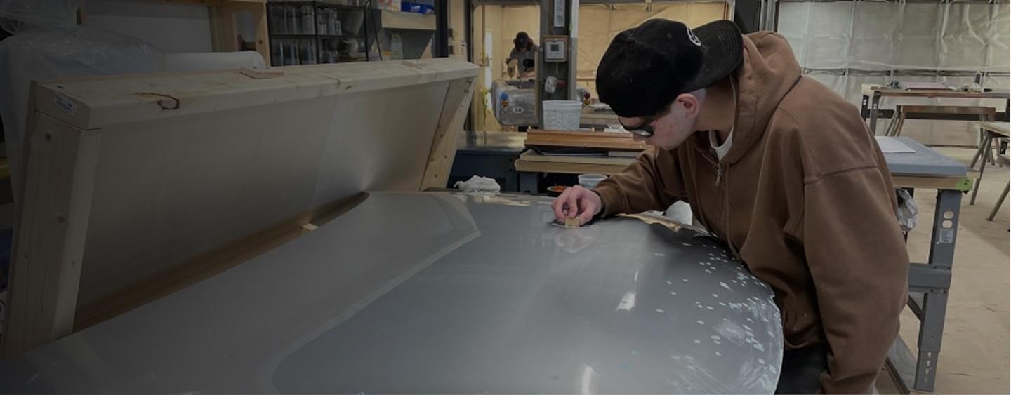 Student carefully sanding a smooth composite surface in a workshop.