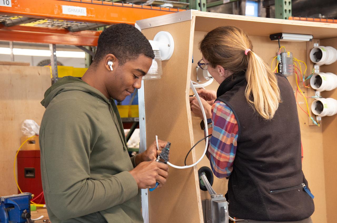 Two people working on an electrical wiring project in a workshop.